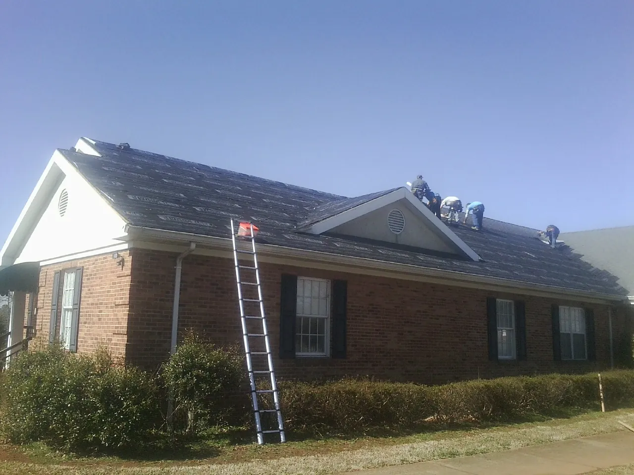 Crew tearing shingles off a brick ranch roof with a ladder set — Emergency Roof Repair work by our crew in Bryn Mawr