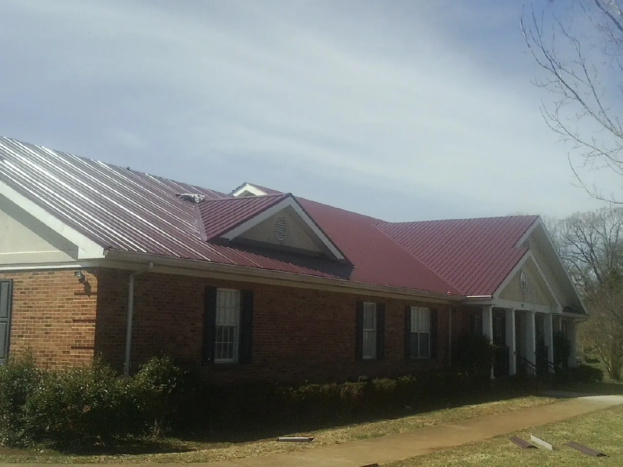 Red metal roof with gabled entries on a long brick building, from a Hail Damage Roof Repair job in Bryn Mawr