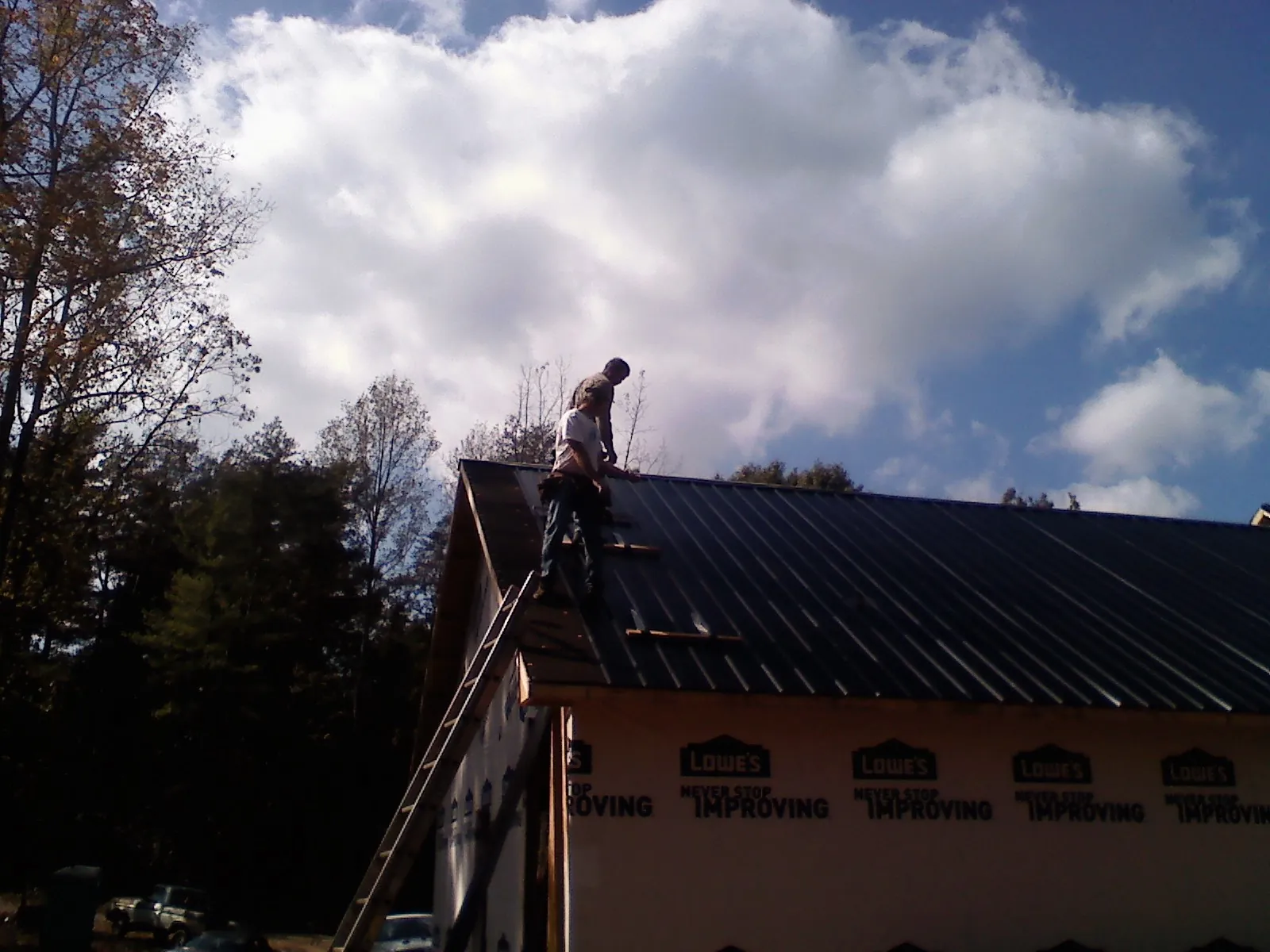 Roofer fastening dark metal panels high against a cloudy sky, from a Roof Inspection job in Bryn Mawr