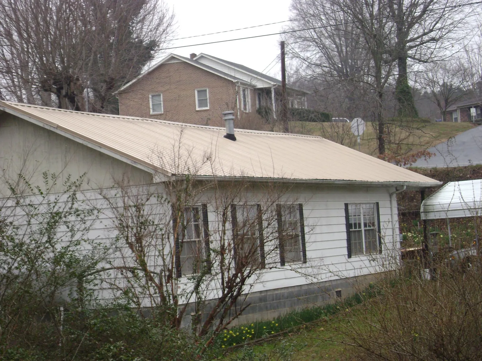 Tan metal roof on a white sided house set into a hillside — Commercial Roofing by Roofing Brothers in Bryn Mawr